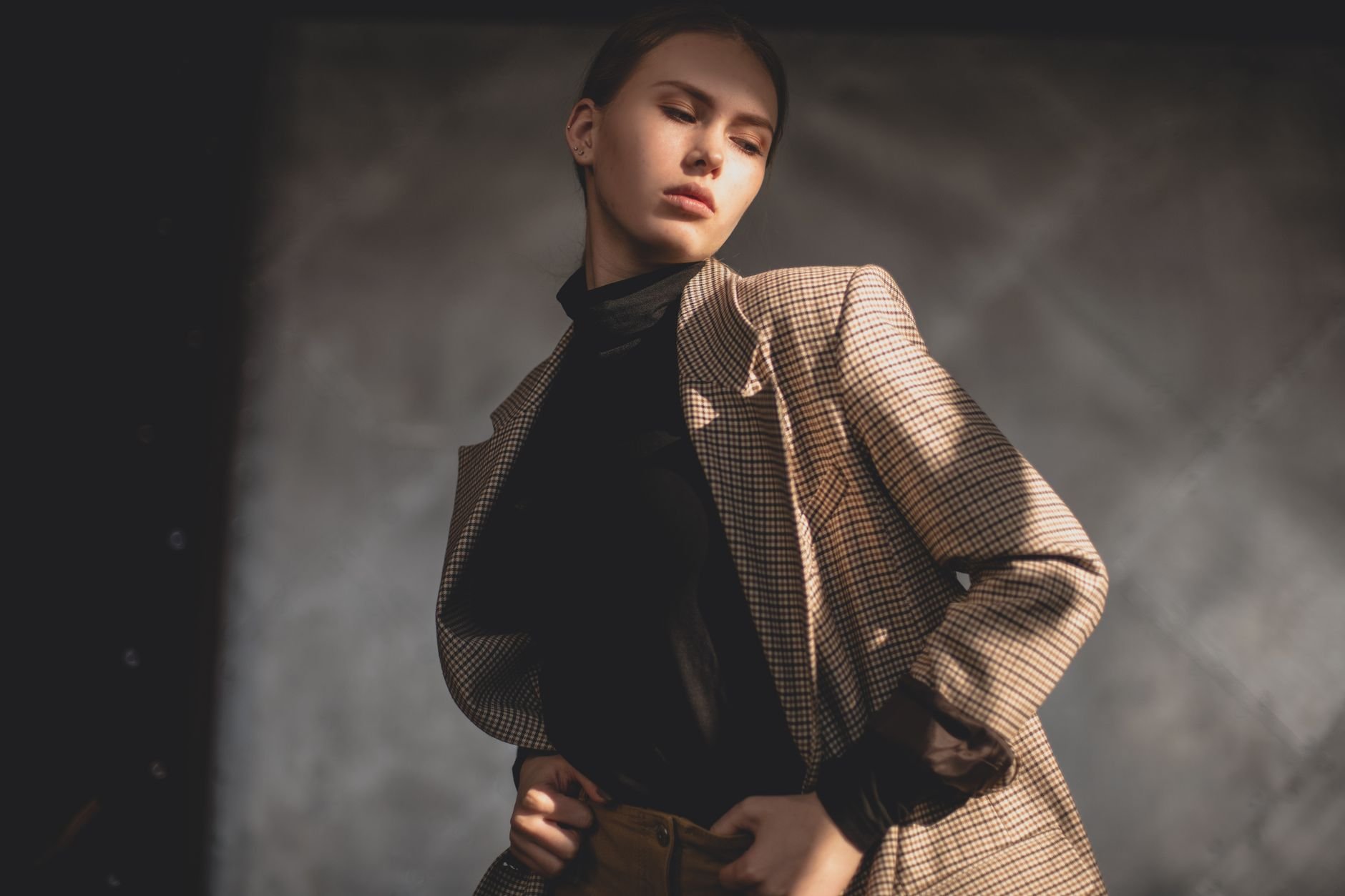 Elegant portrait of a young woman wearing a checkered coat, posing indoors with soft lighting.